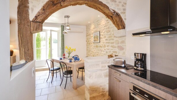 A kitchen with a stone wall, a wooden archway, a dining area with chairs, and a coffee maker. - Stunning home in Montbrison-sur-Lez (Montbrison-sur-Lez)