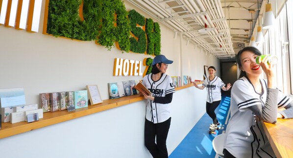 A hotel reception area with a reception desk, a wall-mounted greenery display, and a shelf with informational brochures. - Dash 23 Hotel (Tainan)