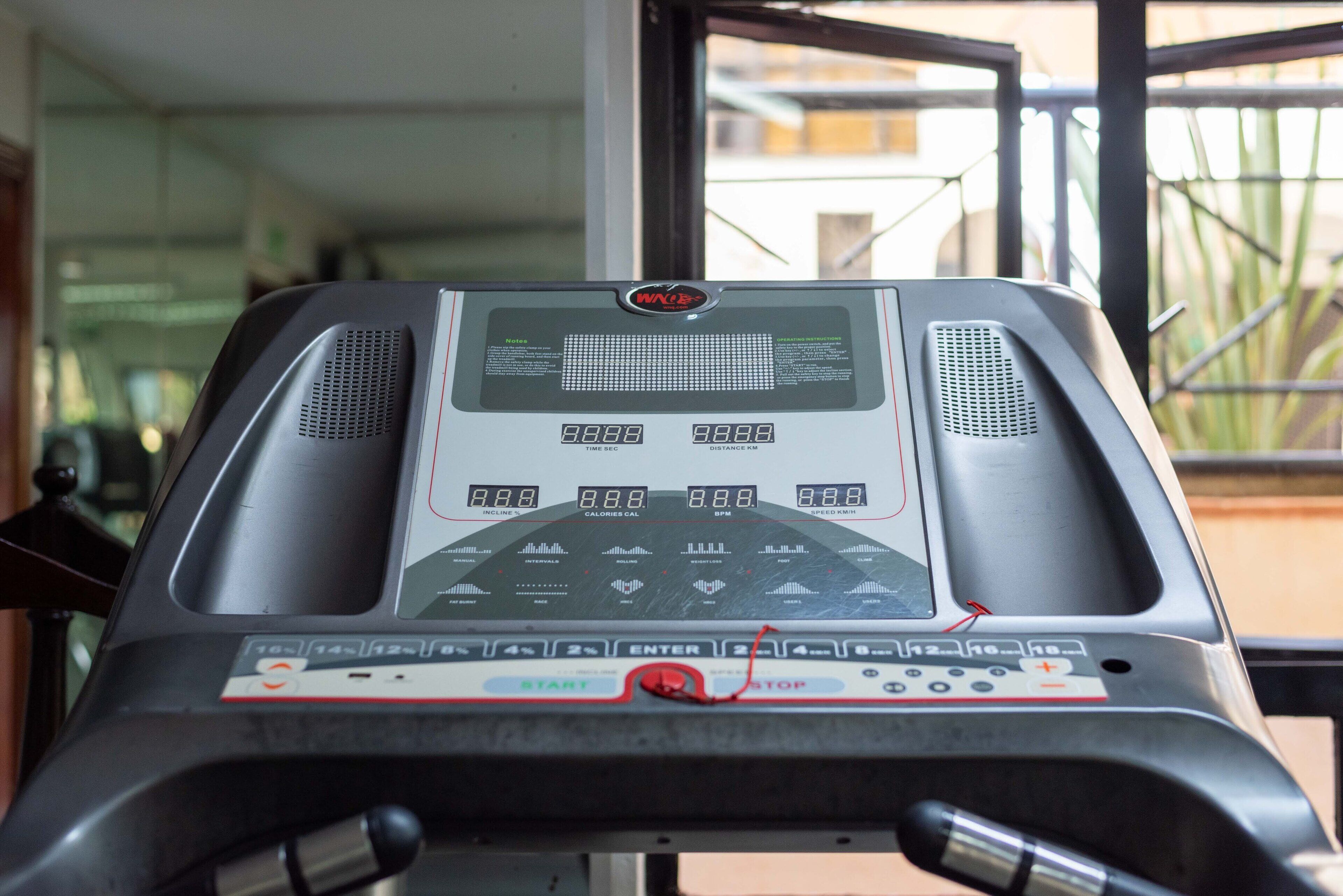 A treadmill with a digital display, control panel, and emergency stop button.