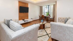 A modern living room with a flat-screen TV, a dining area with a table and chairs, and a large window with curtains. - Cysuites Apartment Hotel (Nairobi)