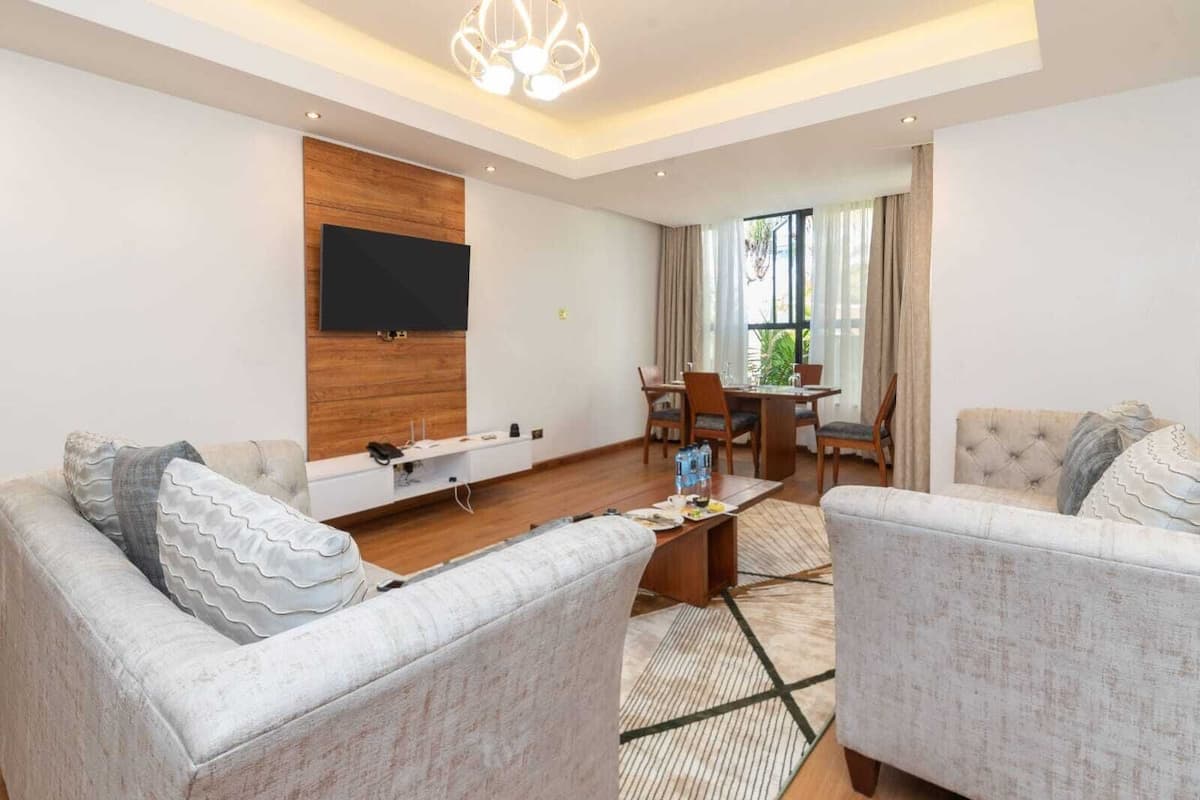 Ein modernes Wohnzimmer mit Fernseher, einem Essbereich mit Tisch und Stühlen sowie einem großen Fenster mit Vorhängen.