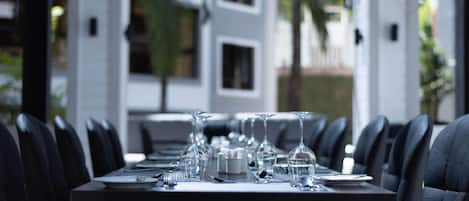 Une table à manger dressée avec des verres à vin, des assiettes et des couverts, entourée de chaises en cuir noir.