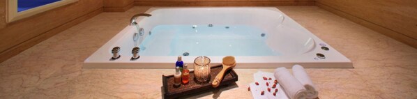 Une baignoire rectangulaire dotée de plusieurs robinets, un plateau en bois contenant des produits de bain et une serviette enroulée posée sur le sol.