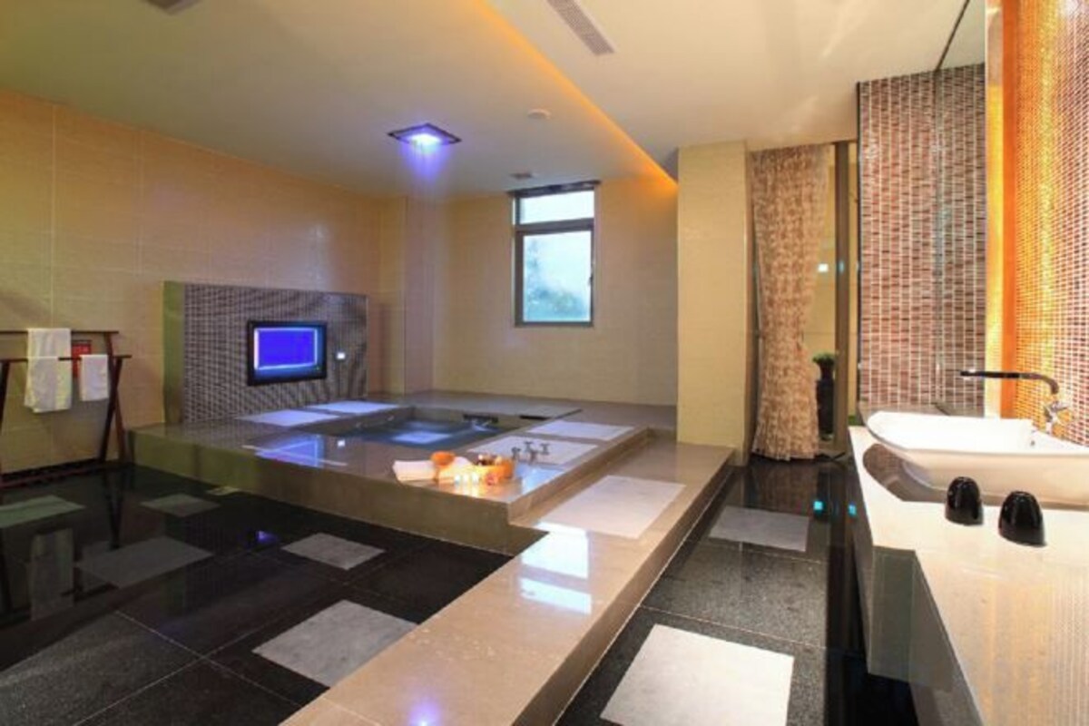 A modern bathroom with a glass-enclosed hot tub, a large mirror, and a separate sink area.