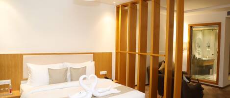 Habitación de hotel con una cama grande, un separador de madera, cabina de ducha con vidrio y una mesita de noche con lámpara.