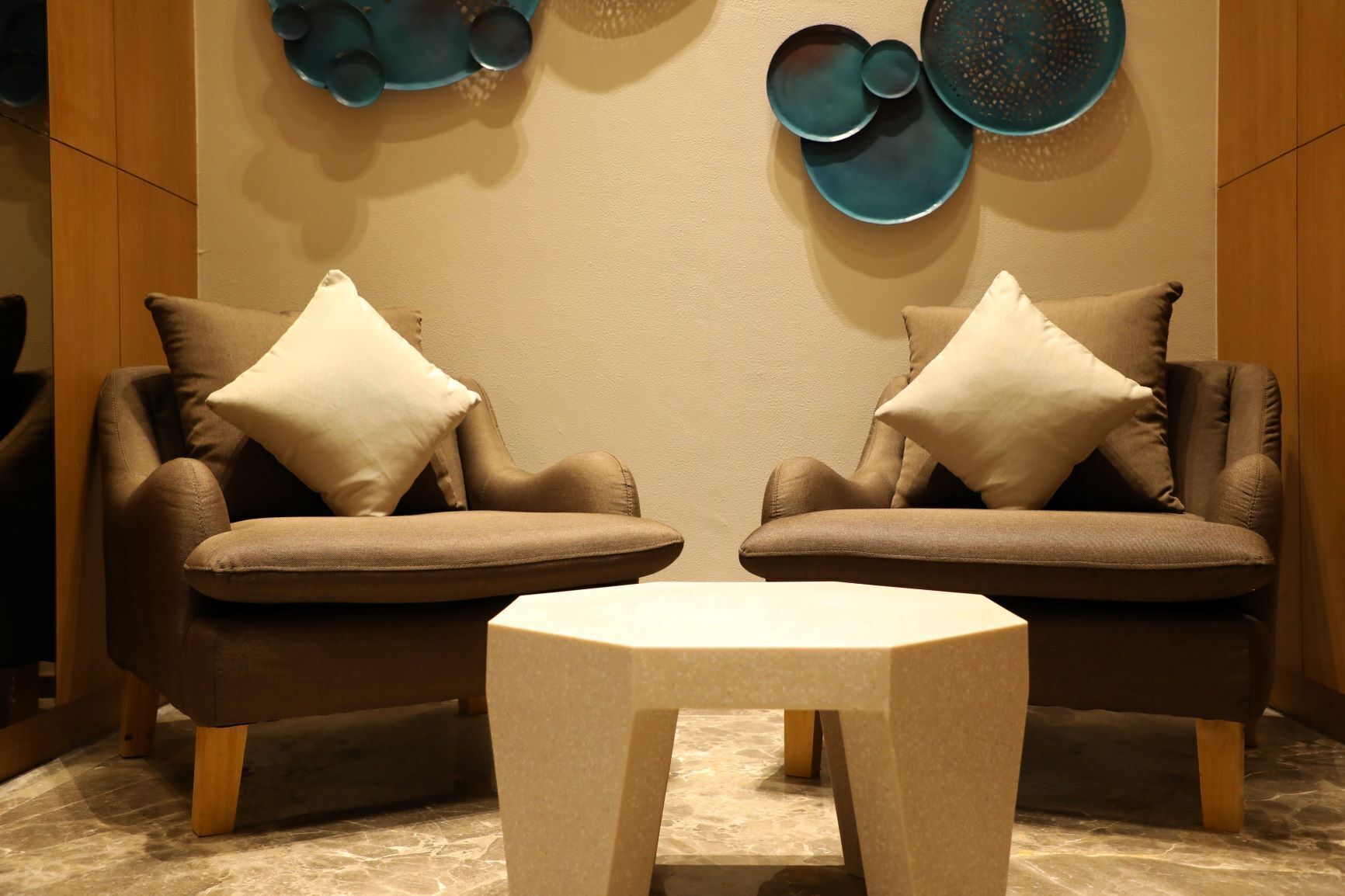 Two brown armchairs with white cushions, a small white table, and decorative wall art.
