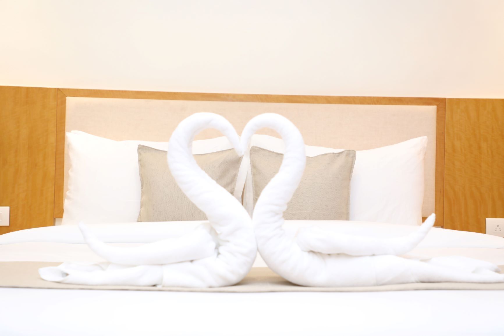 A hotel room with a bed, two pillows, and a towel arrangement in the shape of swans.
