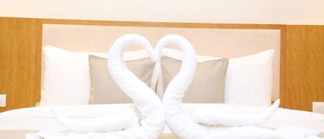 A hotel room with a bed, two pillows, and a towel arrangement in the shape of swans.