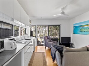 Une cuisine moderne dotée d’un four encastré, un coin repas avec une table et des chaises, et une grande fenêtre offrant une vue sur la forêt.