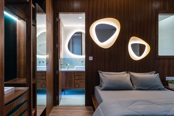 Un dormitorio moderno con un armario de madera, una cama con ropa de cama gris y luminarias fijadas a la pared.
