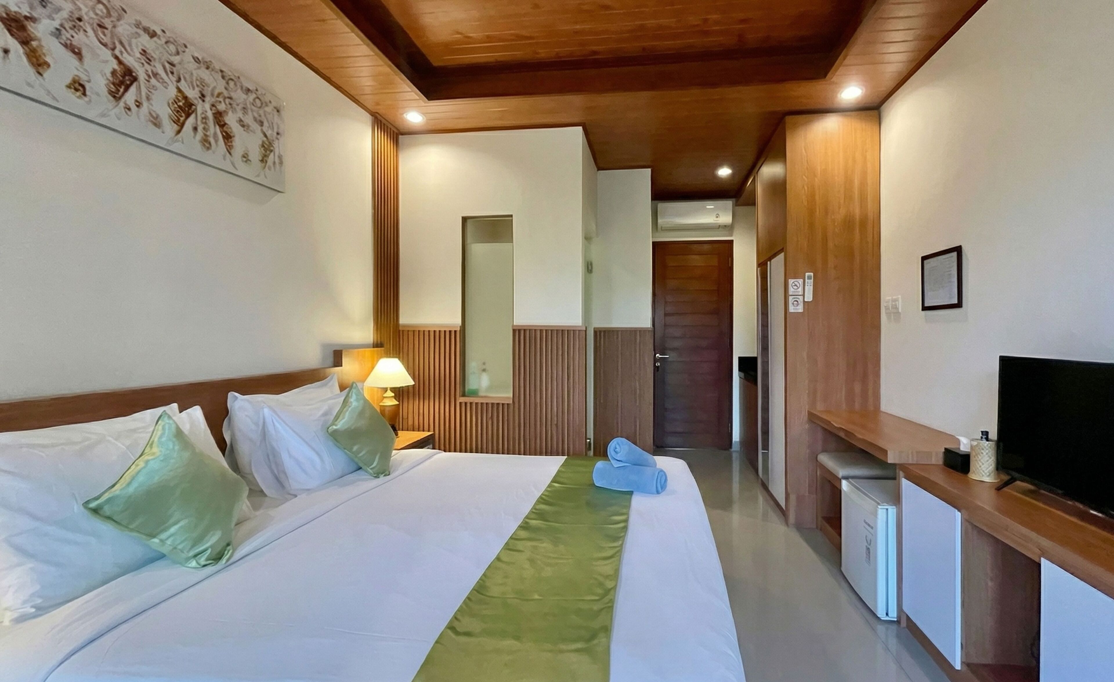 A hotel room with a bed, a desk with a television, a mirror, and a door leading to another room.