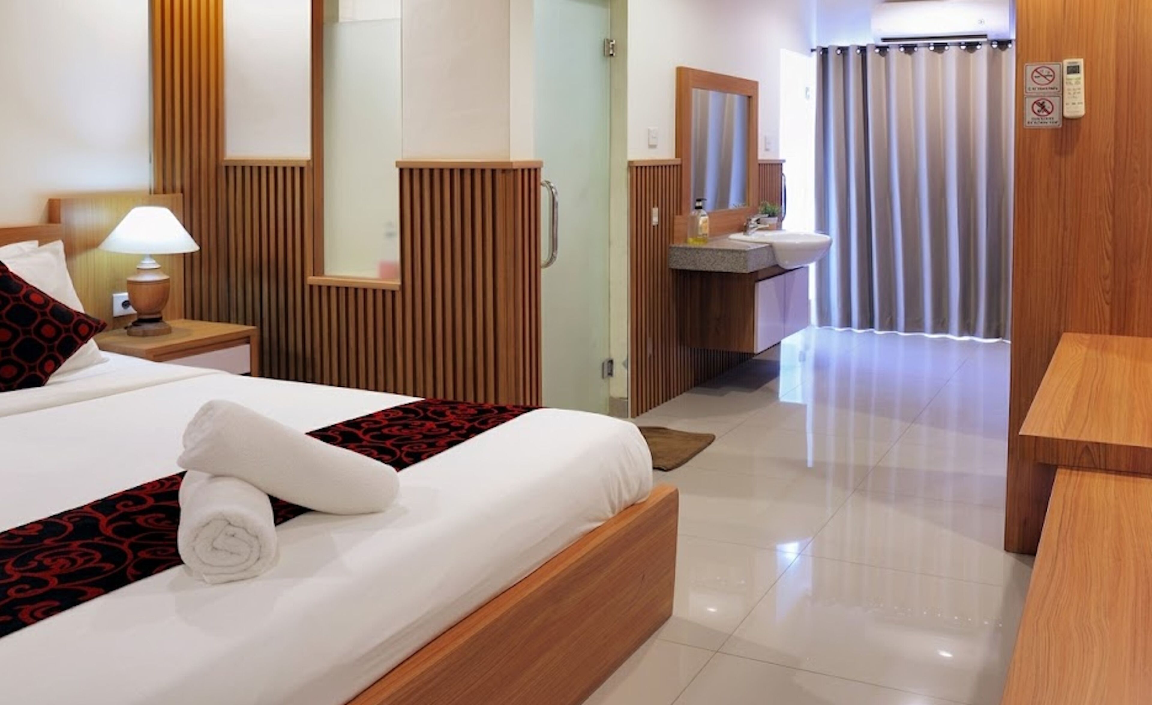 A hotel room with a bed, bedside table, lamp, and a bathroom with a sink and mirror.