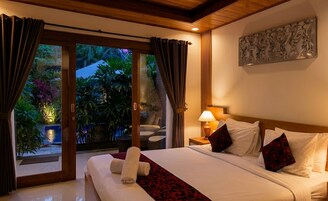 Habitación de hotel con cama, cortinas, mesita de noche, lámpara y vista a un jardín.