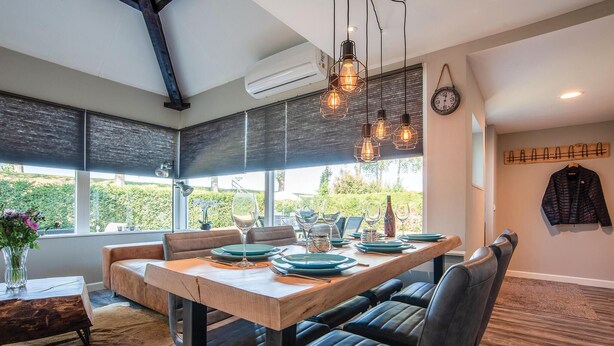 A dining area with a wooden table, leather chairs, and pendant lighting. - Oud Kempen Bungalow 99 (Stavenisse)