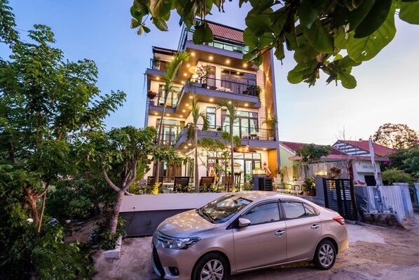 A multi-story building with balconies, a car parked in front, and surrounding greenery. - Ancient River Villa (Da Nang)