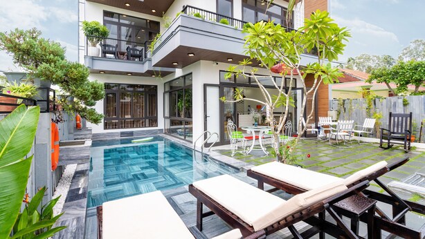 A modern building with a swimming pool, outdoor seating, and lush greenery. - Ancient River Villa (Da Nang)