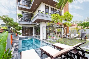 A modern building with a swimming pool, outdoor seating, and lush greenery. - Ancient River Villa (Da Nang)