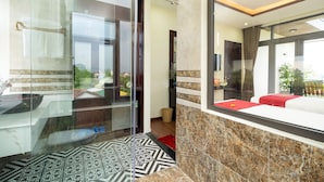 A modern hotel room with a glass partition, a bed with red bedding, a red rug, and a view of the outdoors. - Ancient River Villa (Da Nang)