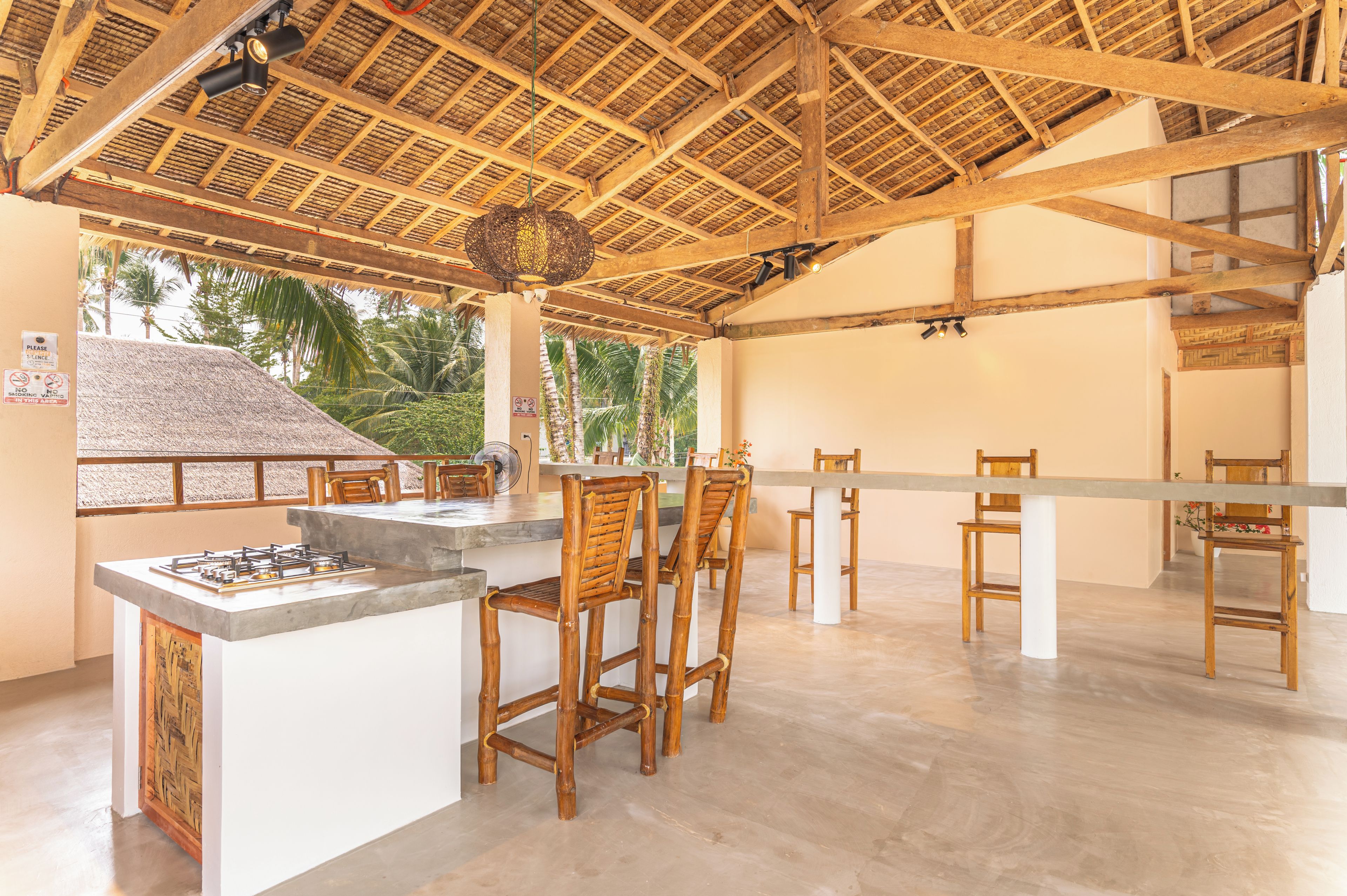 An outdoor dining area with a thatched roof, wooden furniture, and a central island with a gas stove.