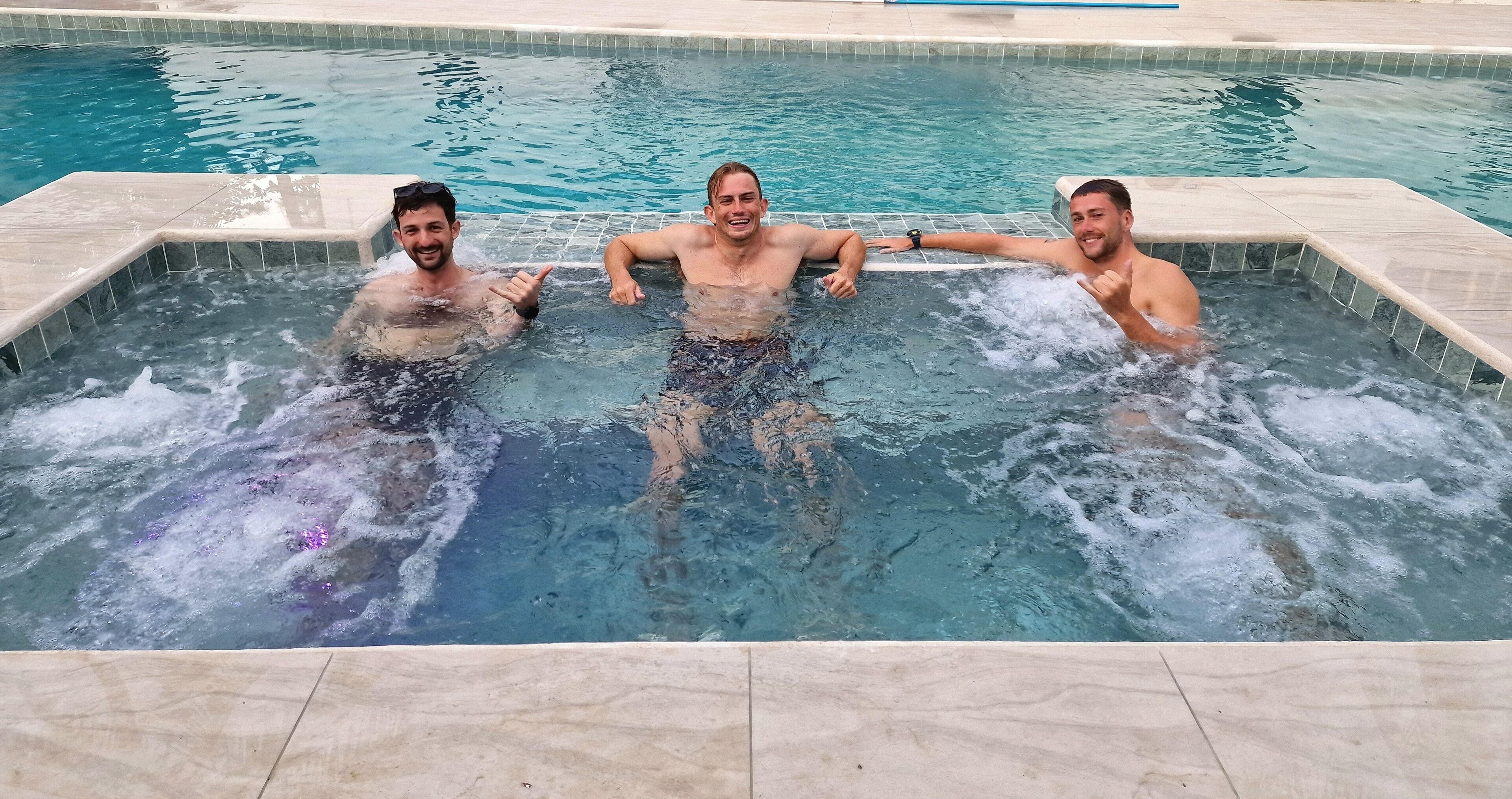 Tres personas en un jacuzzi con agua cristalina y bordes de azulejos.