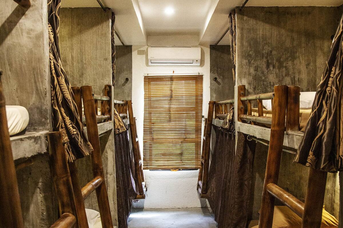 A narrow corridor with bunk beds on either side, a concrete floor, and a wooden door at the end.