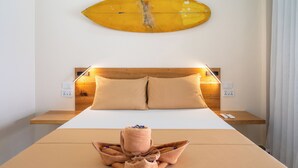 A hotel room with a bed, a wooden headboard, a wall-mounted surfboard, and a towel with flowers. - Sunlit Hostel (General Luna)