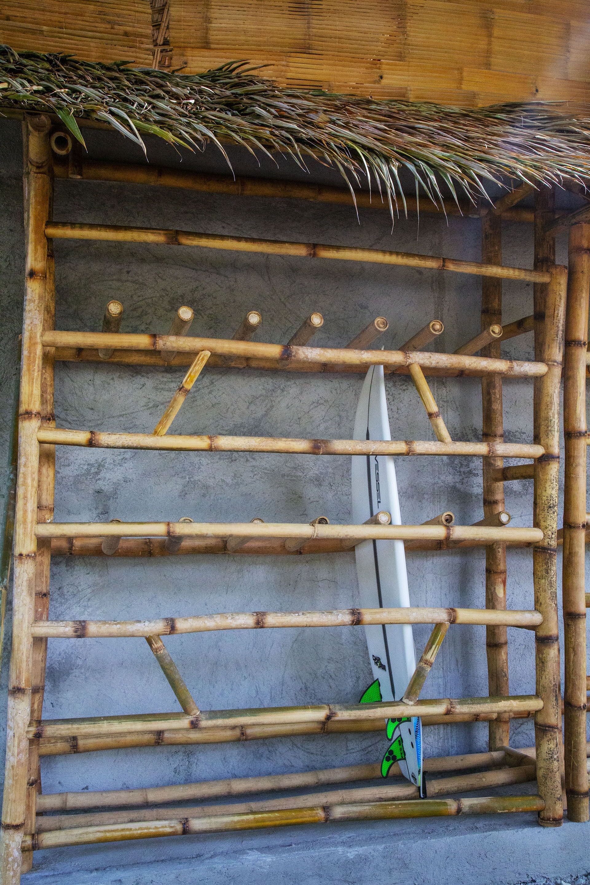 Un estante de bambú con tablas de surf apoyadas contra una pared de hormigón.