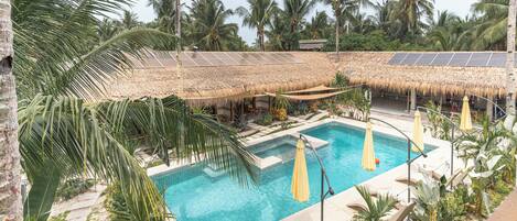 A pool area with a thatched roof, solar panels, and tropical vegetation.