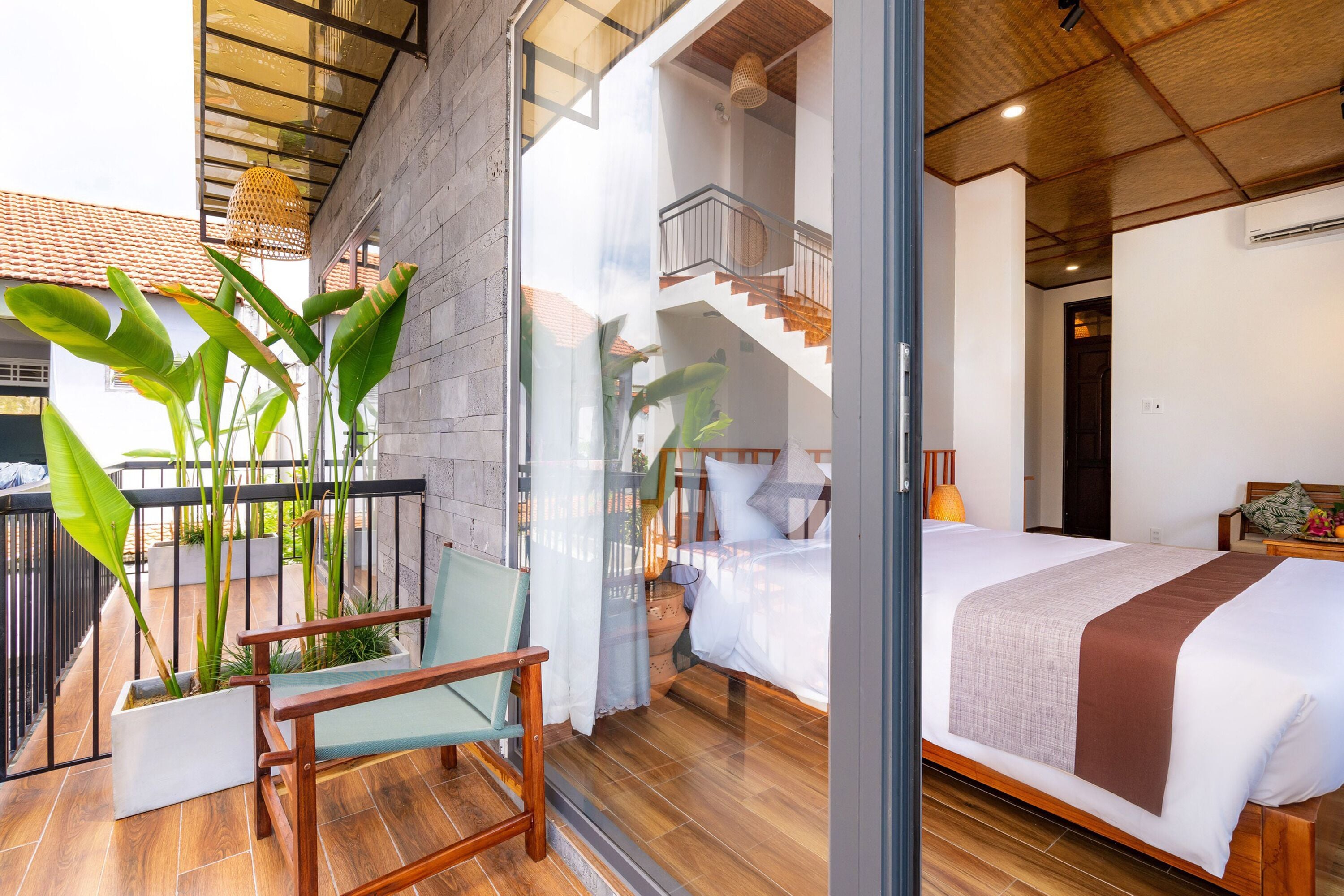 A modern bedroom with a large bed, a balcony with plants, and a staircase leading to an upper level.