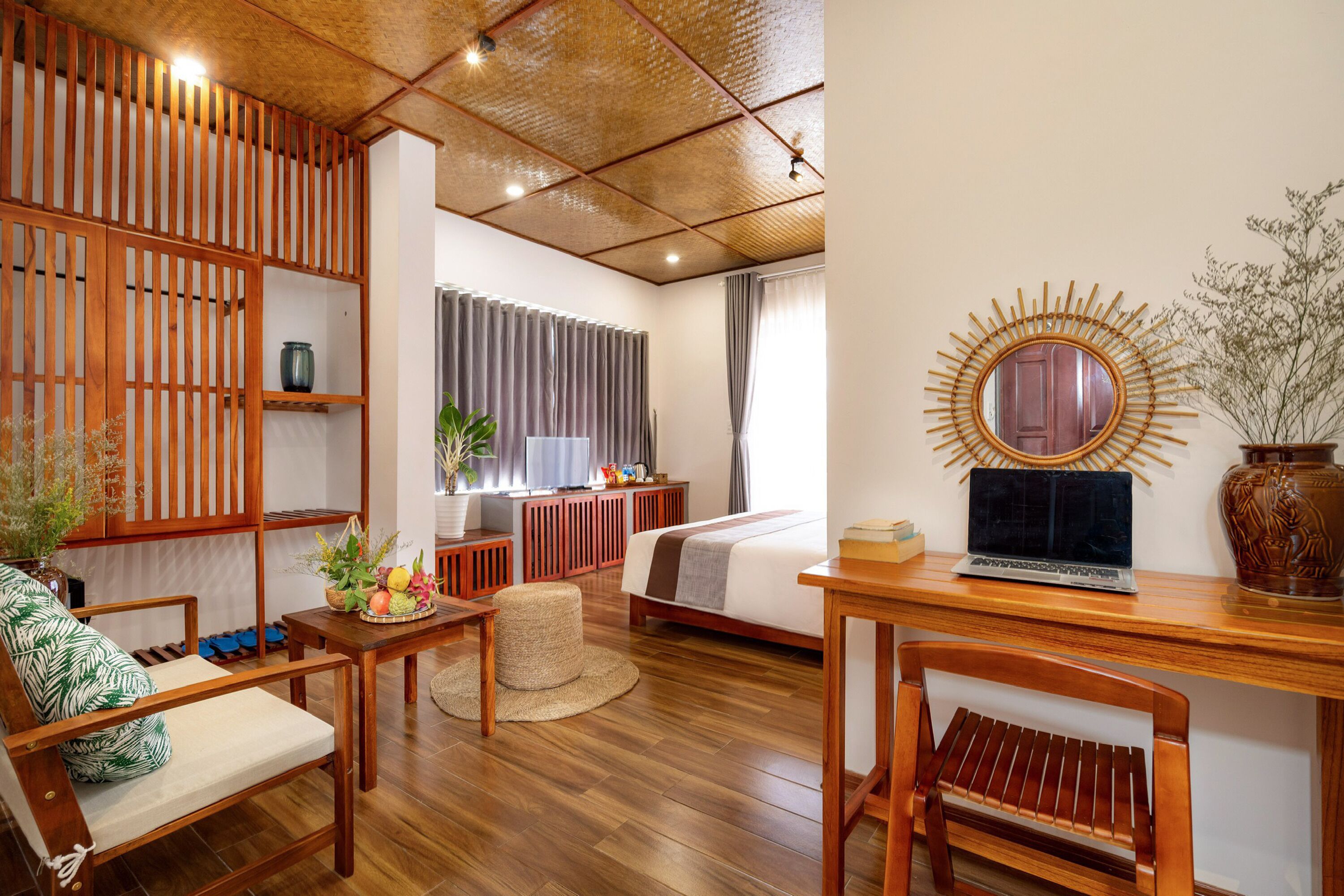 Habitación de hotel moderna con piso de madera, una cama, un escritorio con una computadora portátil, un espejo grande y una planta en maceta.