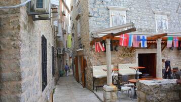 A narrow street with stone buildings, outdoor seating, and flags.