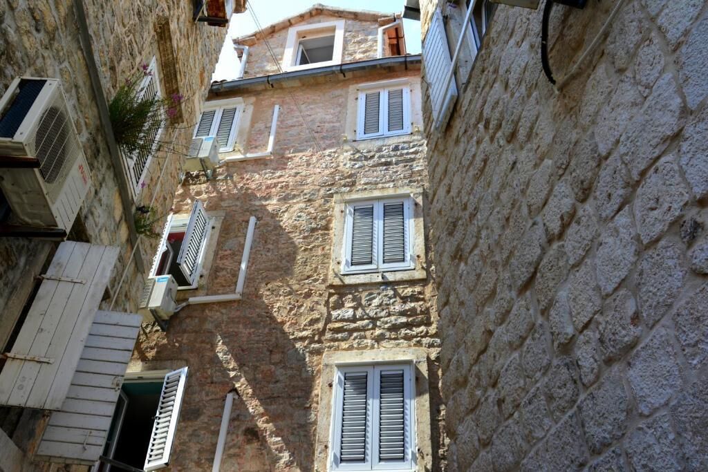 A narrow street with stone buildings, multiple windows, and air conditioning units.