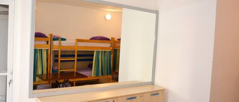 A dormitory room with bunk beds, a mirror, and a wooden cabinet.