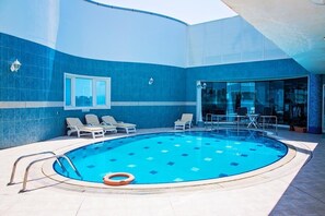 Une piscine aux carreaux bleus, dotée de chaises longues et d’une entrée avec une porte en verre.