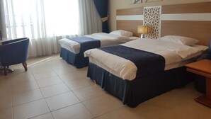 Een hotelkamer met twee bedden, een stoel, een tafel en een raam met gordijnen.