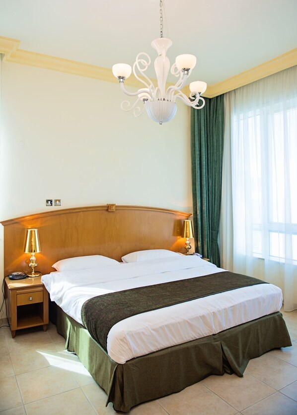 Hotelkamer met een groot bed, twee bedlampen, een kroonluchter en uitzicht door gordijnen.