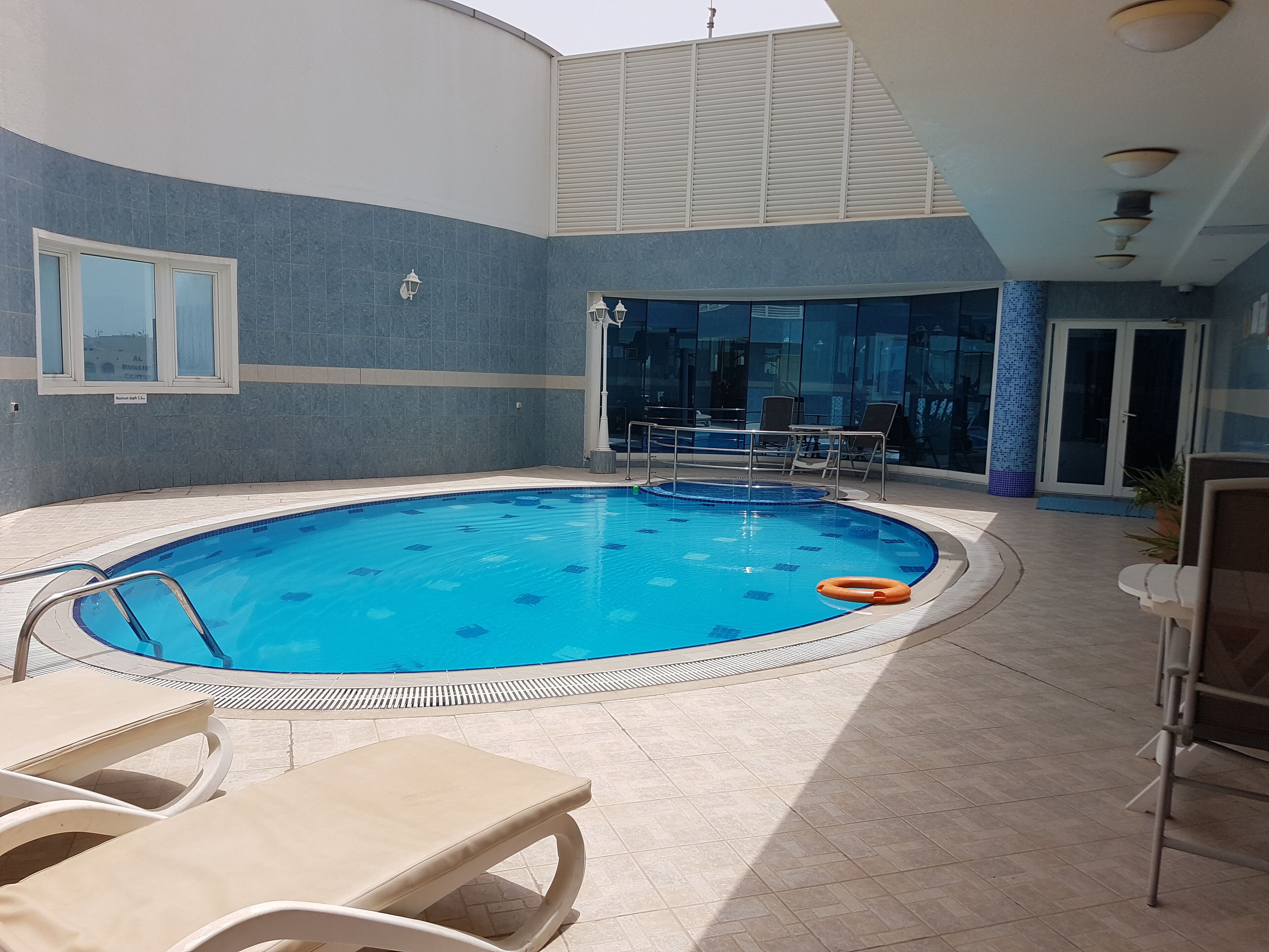 Une piscine intérieure avec un sol carrelé, des chaises longues et une porte vitrée donnant sur un espace ext érieur.