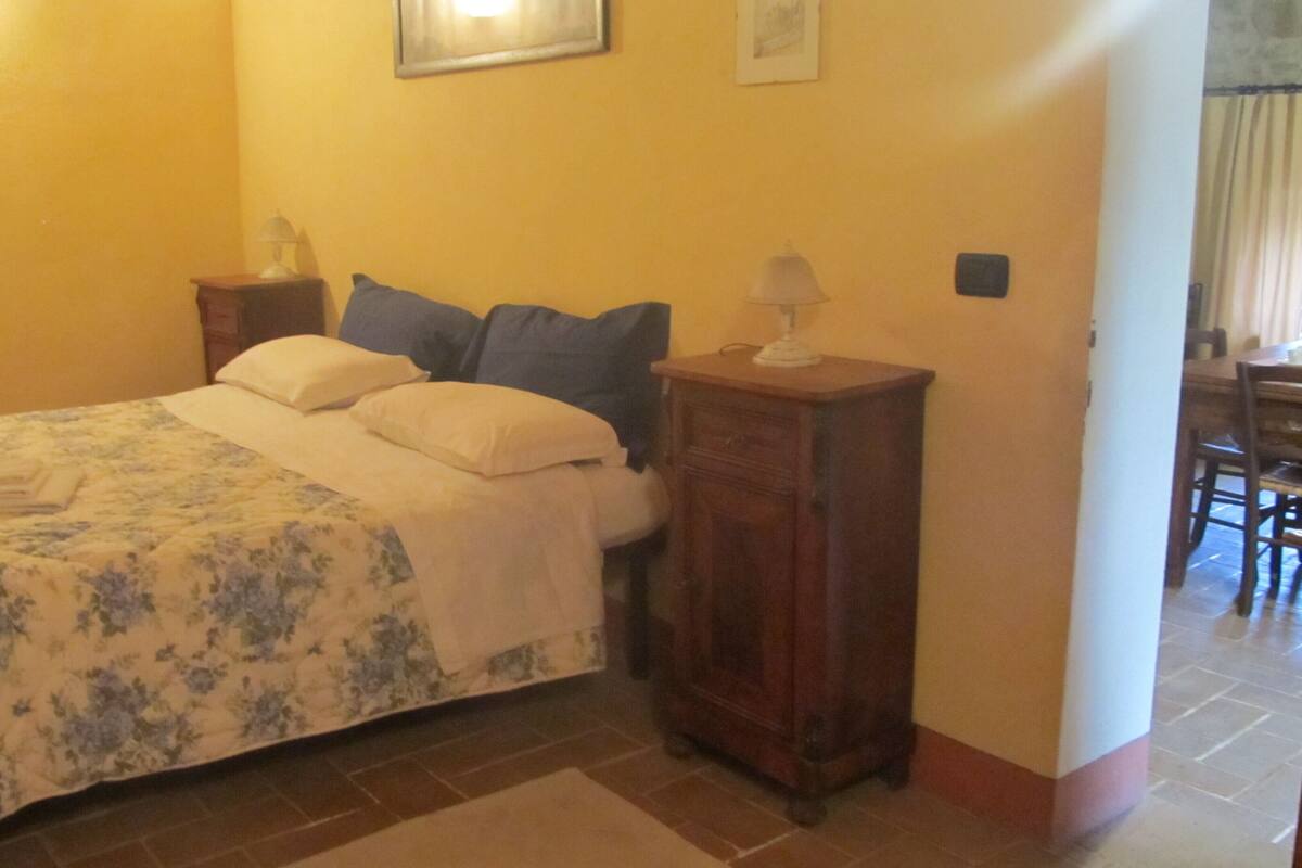 Un dormitorio con una cama, dos mesitas de noche, un aparador y un armario, además de una puerta que da a un comedor.