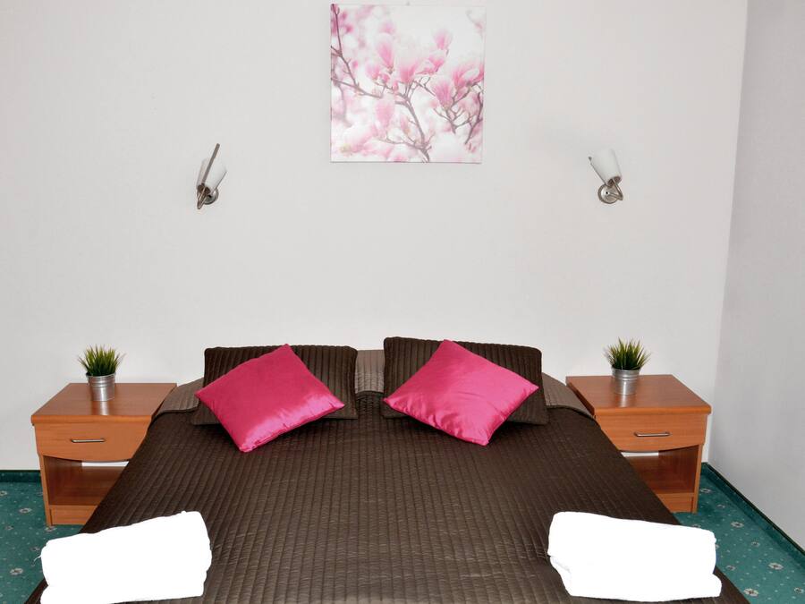 Een keurig opgemaakt slaapkamer met een groot bed, twee nachtkastjes met planten en een aan de muur hangend schilderij.