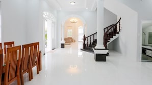 A spacious, well-lit interior with a polished floor, a staircase with wooden railings, and a dining area with wooden chairs. - 7S Hotel Lam Villa & Resort (Ho Chi Minh City)