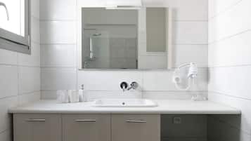 Un baño moderno con un lavamanos blanco, un espejo y una ducha. Hay una cesta de mimbre en el suelo.