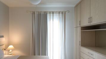 Une chambre à coucher comprenant un lit, une table de chevet avec une lampe, une fenêtre avec des rideaux et des armoires encastrées en bois.