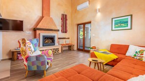 A living room with a fireplace, orange sofas, a colorful chair, and a framed landscape painting on the wall. - Pool, grill, WiFi, bicycles, billiards, dishwasher, washing machine (Loborika)