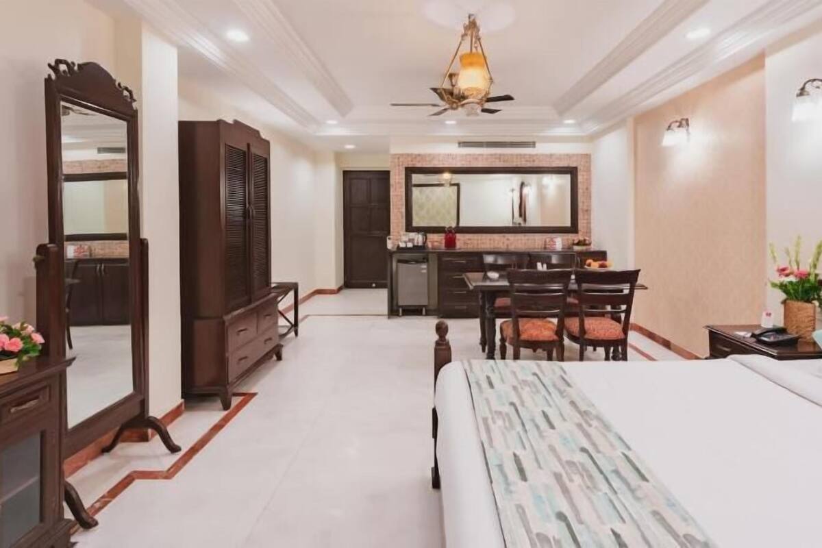 A hotel room with a bed, a desk, a chair, a wardrobe, a mirror, and a ceiling fan.