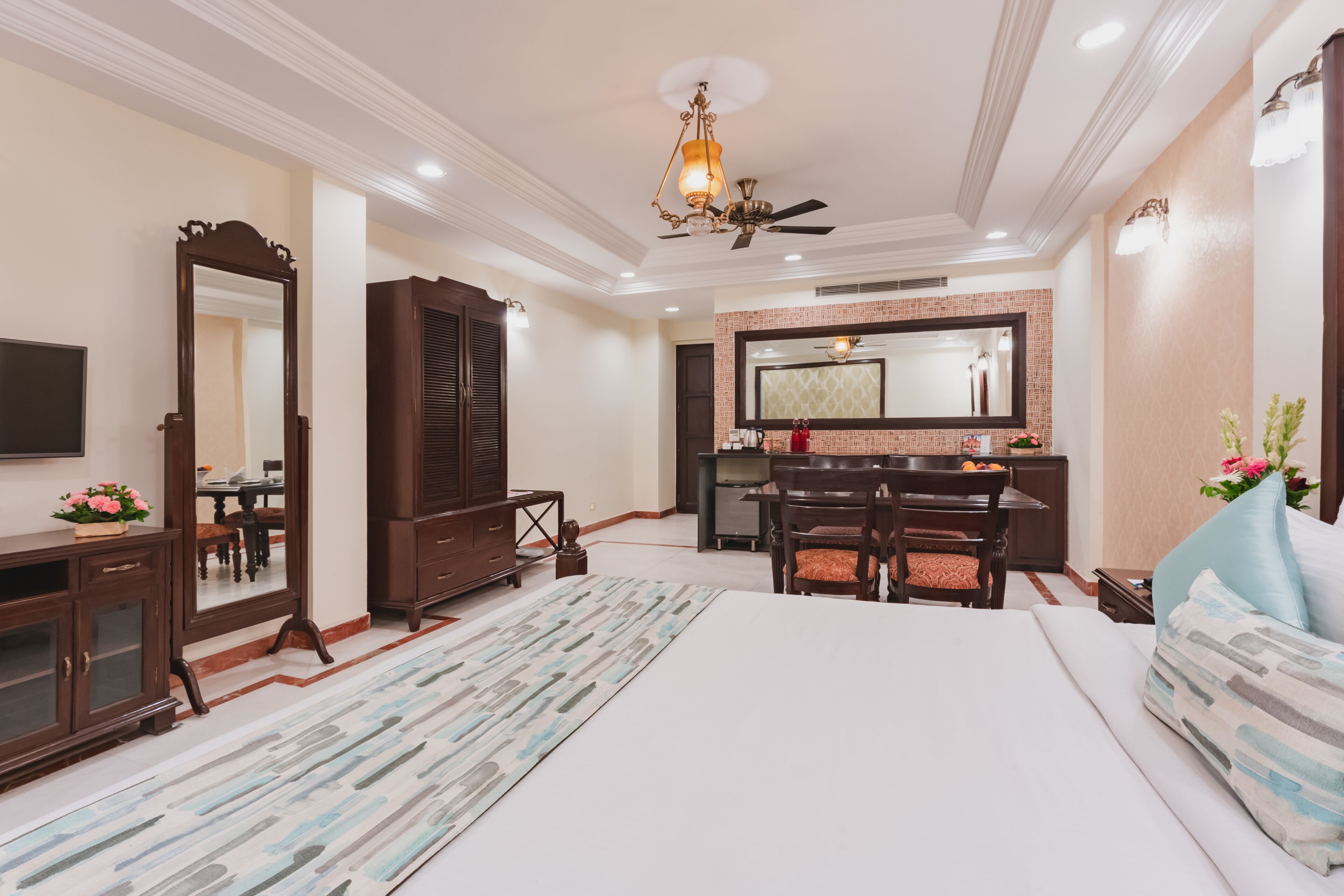 A hotel room with a large bed, a desk with a chair, a dresser, a mirror, and a ceiling fan.