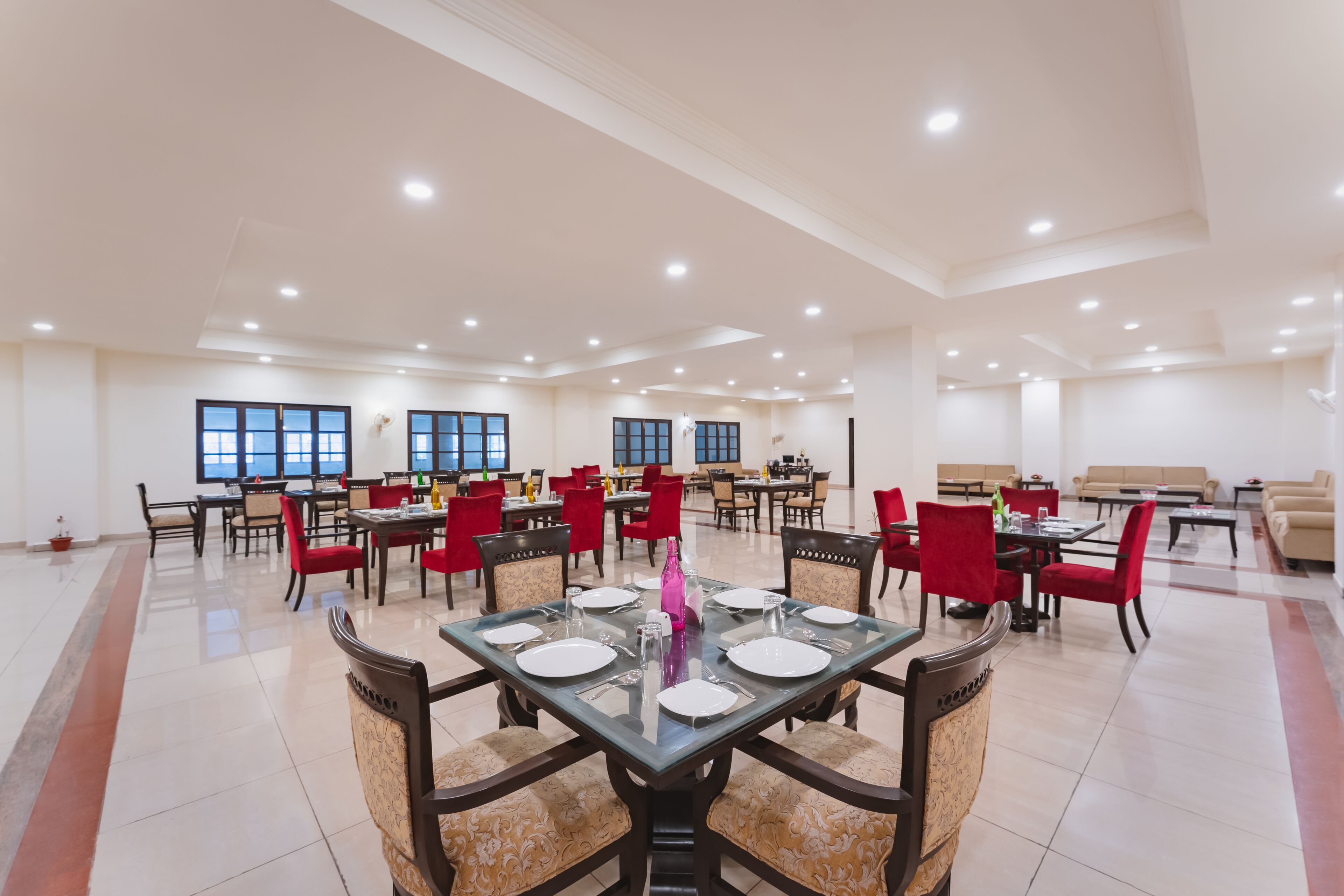 A spacious dining area with multiple tables and chairs, large windows, and a modern ceiling design.