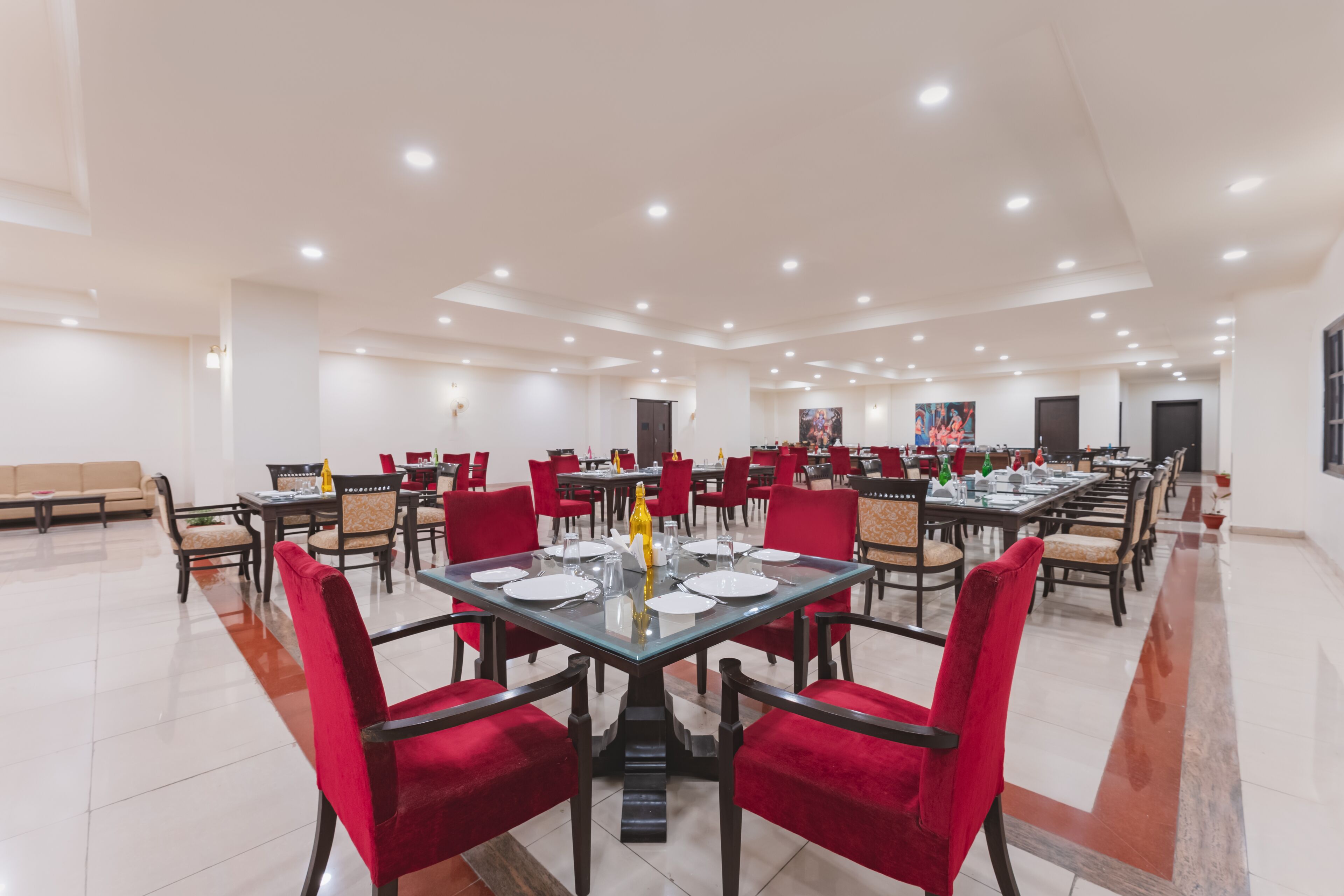 A spacious dining area with multiple tables and red chairs, featuring a modern ceiling design with recessed lighting.