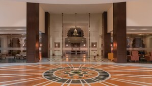 Een ruime lobby met een centrale kroonluchter, grote pilaren en een vloer met een patroon.