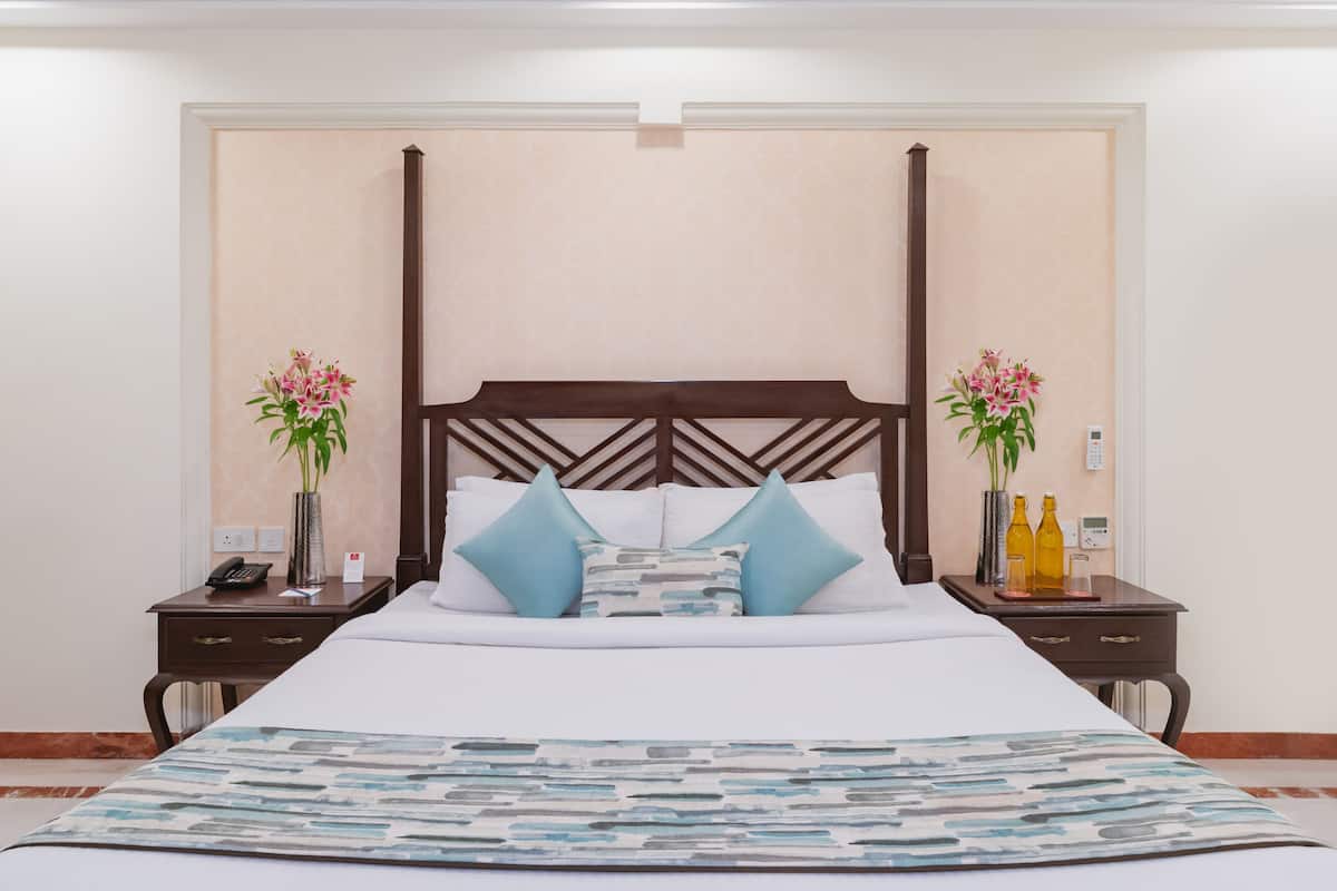A hotel room with a large bed, two bedside tables, a nightstand, and a wall-mounted control panel.