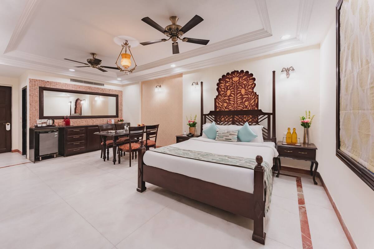 A spacious bedroom with a large bed, a desk, and a chair, a ceiling fan, and a decorative wall panel.
